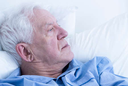 Elderman lying on a hospital bed and looking into spaceの写真素材