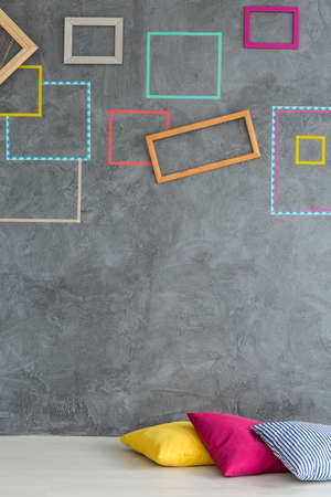 Colorful decorative frames on a grey wall and three pillows