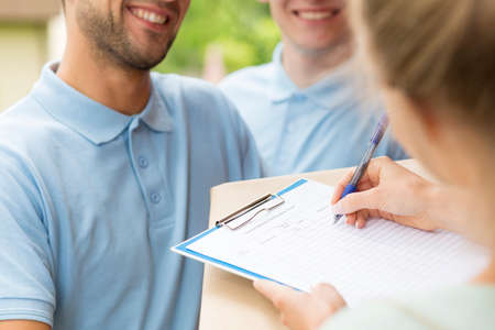 Close up of a two couriers with a parcel and woman signing a delivery formの写真素材