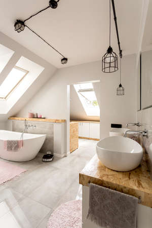 Bright interior of bathroom with minimalistic lighting, roofwindows, white amenities and oval bathtubの写真素材
