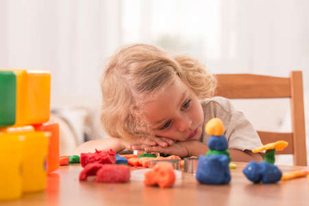 Bored girl leaning her head on the table with plasticine toys on it