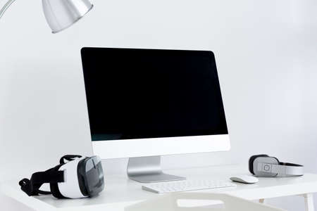 Minimalistic desktop with the monitor screen, type and earphones on itの写真素材