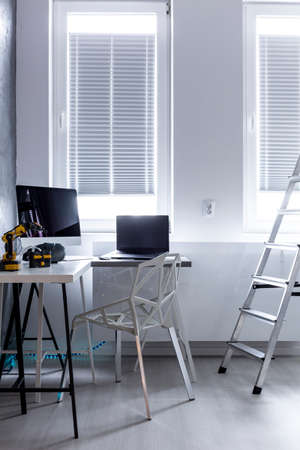 Bright room interior with two windows, computers and robots on the desktop and the ladder