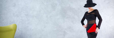 Elegant woman in black dress, with black hat eclipsing her eyes and red clutch in her handの写真素材