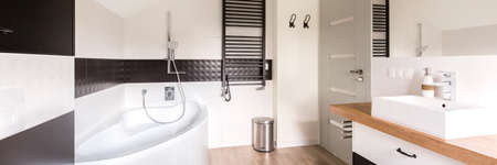 Minimalist and modern bathroom in black and white, with corner bath, black heater and rectangular handbasinの写真素材