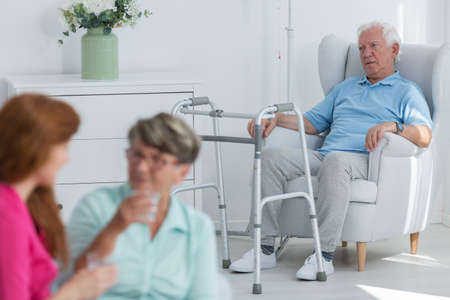 Disabled man with walker sitting in armchair