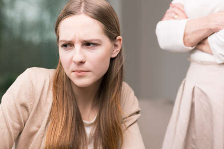 Sad teenage girl , in the background woman standing with her arms crossedの写真素材