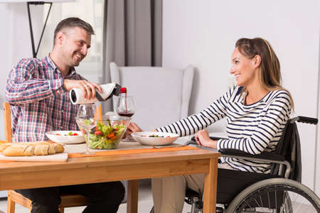 Man pours wine to glass of woman on a wheelchair at the common mealの写真素材