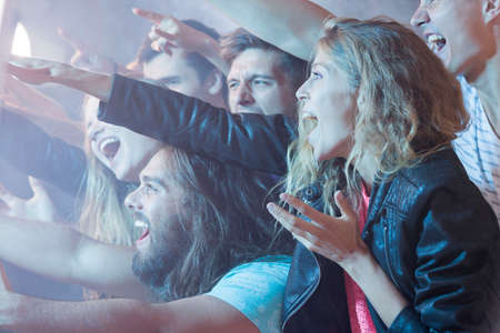 Young girl standing in a crowd of people, having fun at a rock concertの写真素材