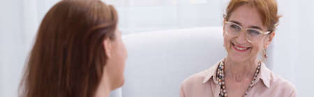 Joyful therapist looks pleased on smile of her happy female patient after successful sessionの写真素材