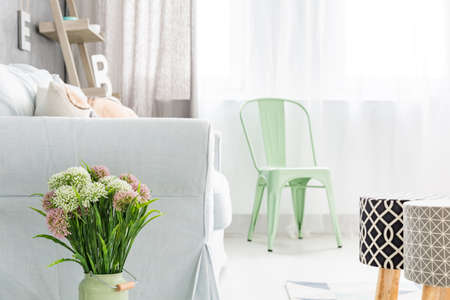 Light room with upholstered stools, sofa, green chair and flowersの写真素材