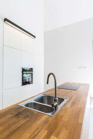 Modern minimalist kitchen with white walls, built-in cabinets and wooden table topの写真素材
