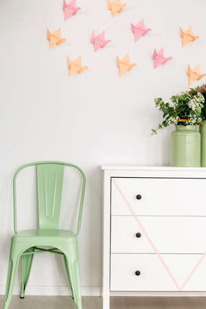 View of mint chair standing next to the white commode in bright room