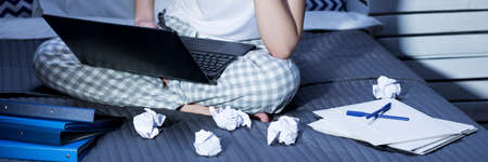 Woman in pajamas sitting in bed and working on laptop at nightの写真素材