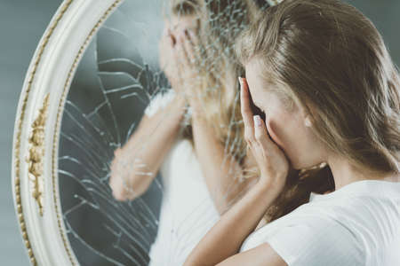 Woman with mental problems covering her face reflected in mirrorの写真素材