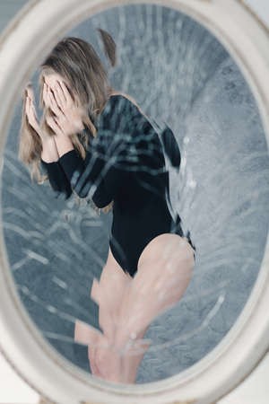 Reflection of anorexic girl in a round broken mirrorの写真素材