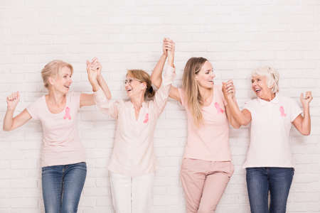 Positive cancer survivors wearing pink, holding each other handsの写真素材
