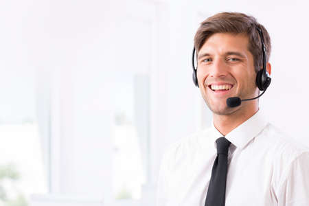 Smiling young call-center employee with headphones with the microphone