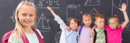 Happy school girl and group of children, chalkboard in the backgroundの写真素材