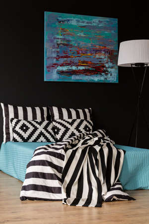 Modern bedroom with bed, blue painting and lamp
