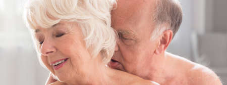 Close-up of happy elderly naked woman kissing with passion by her senior husbandの写真素材