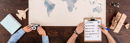 Top view of woman holding a camera and man making notes for trip sitting over a world mapの写真素材