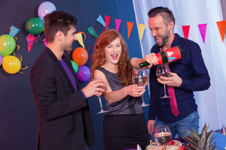 Two men and woman pouring glass of champagne during partyの写真素材