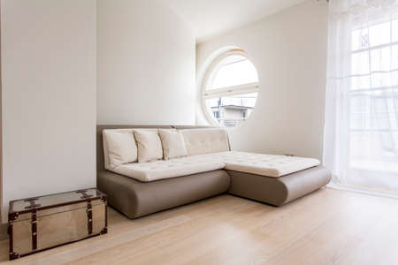 Bright guest room with a sofa bed and big round windowの写真素材