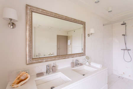 Minimalist bathroom with large mirror in a decorative frame and two marble sinks