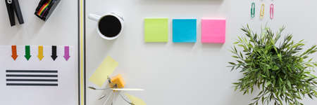 Top view of office accessories like sticky notes, clips and adhesive tape and coffee on white deskの写真素材