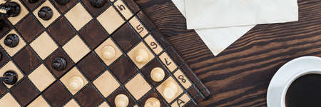 Panoramic close-up of wooden chess set, papers and cup of coffee on mahogany deskの写真素材