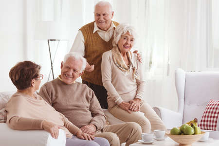 Two senior couples relaxing together at home, talking and smilingの写真素材