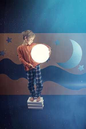 Boy wearing pajama holding glowing ball, night sky in backgroundの写真素材