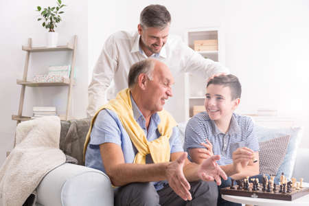 Grandfather and grandson playing chess, father watching them smilingの写真素材