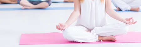 Woman in white clothes meditating at pink yoga mat during yoga classの写真素材
