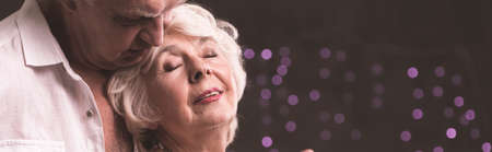 Panorama of senior elegant man embrancing elderly woman with bookeh backgroundの写真素材