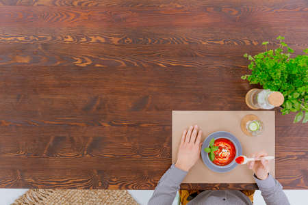 Person sitting beside rustic table eating red cream soupの写真素材