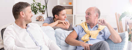 Young son, middle aged father and senior grandfather sitting together in lounge