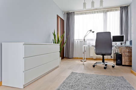 Modern grey home office with white commode, desk with computer and chairの写真素材