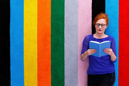 Young woman laying on colorful carpet and reading a bookの写真素材