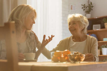 Woman sitting beside table while talking with her old motherの写真素材