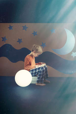 Young boy reading a book at nightの写真素材