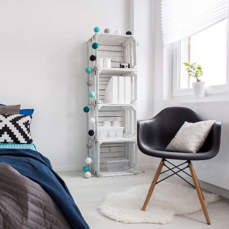 New minimalist interior with white walls, big bed, black chair and DIY white regale
