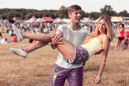 Happy man holding in his arms a beautiful girlfriend, having fun during summer festivalの写真素材