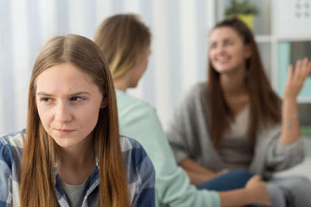 Sad young girl sitting with friends talking in the backgroundの写真素材