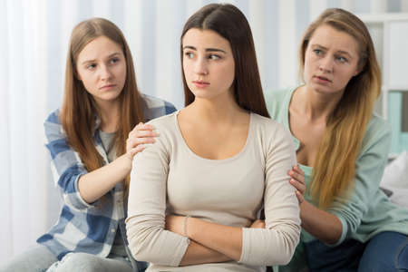 Thoughtful female teenager being supported by her worried friendsの写真素材