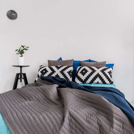 Gray bedcover on the bed in minimalist modern bedroom with white walls
