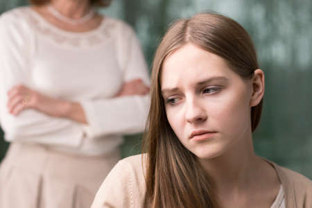 Sad teenage girl suffering from depression with mother in the backgroundの写真素材