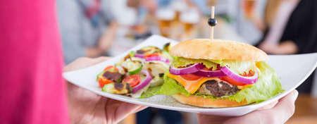 Woman holding a white plate with burger and saladの写真素材
