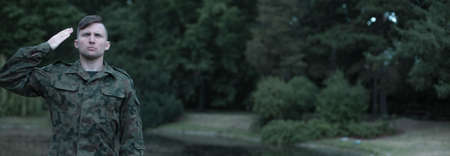 Panoramic view of a young soldier wearing military uniform salutingの写真素材